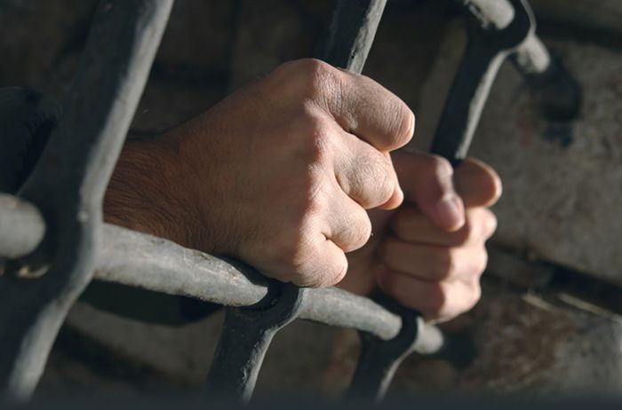 Руки заключенного держатся за прутья решетки